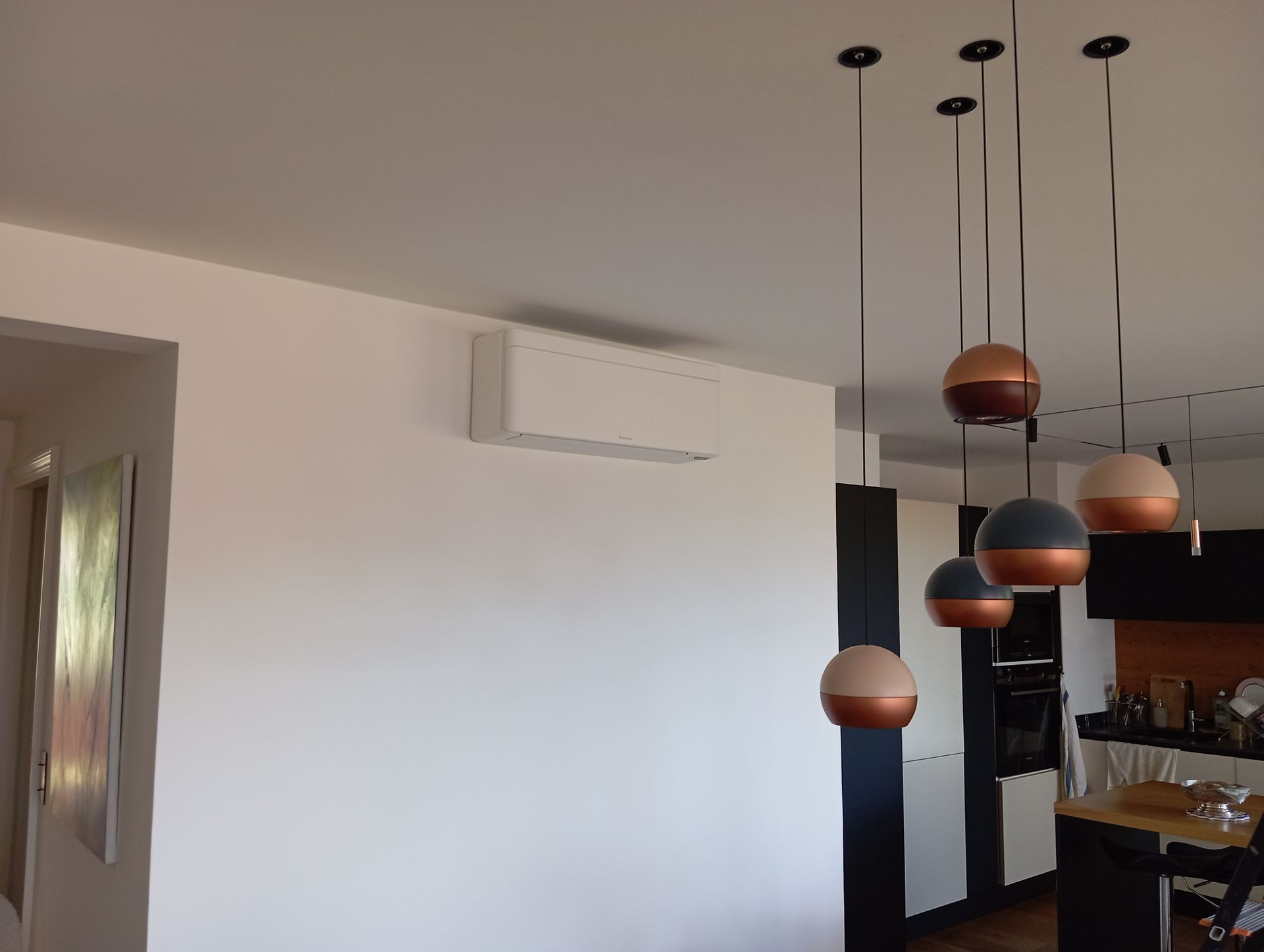 Mur blanc avec climatiseur, luminaires suspendus avec sphères en cuivre et bleu marine et coin cuisine.