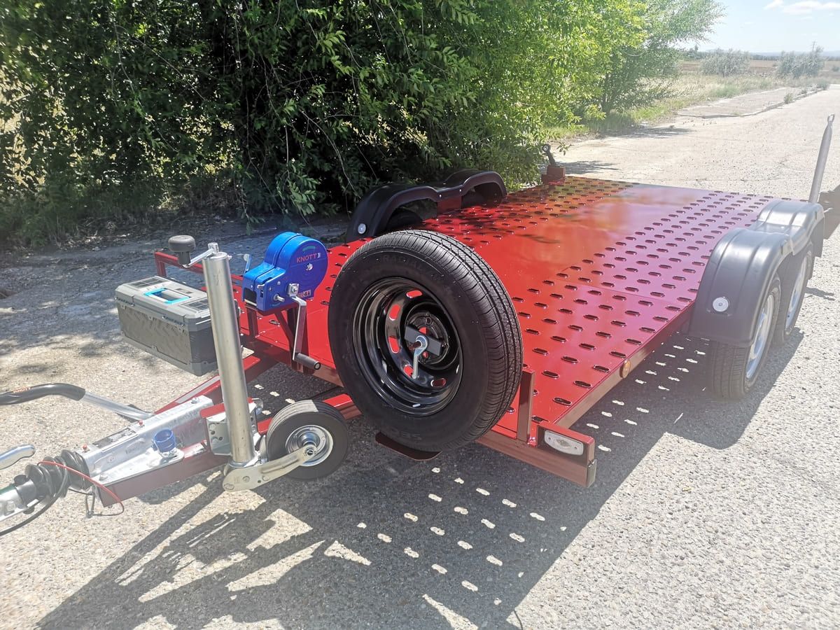 Un remolque rojo está estacionado al costado de la carretera al lado de un árbol.