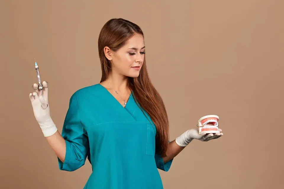 Profesional dental con bata turquesa sosteniendo una jeringa y un modelo dental sobre un fondo liso.