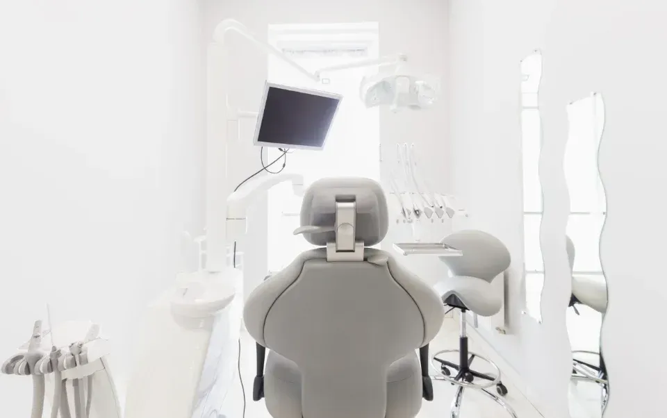 Clínica dental luminosa con sillón, monitor e instrumental en una sala de tratamiento blanca.