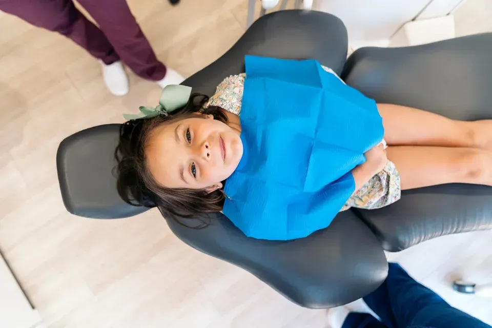 Un niño está tumbado en el sillón dental durante una revisión, lleva un babero azul brillante y sonríe.