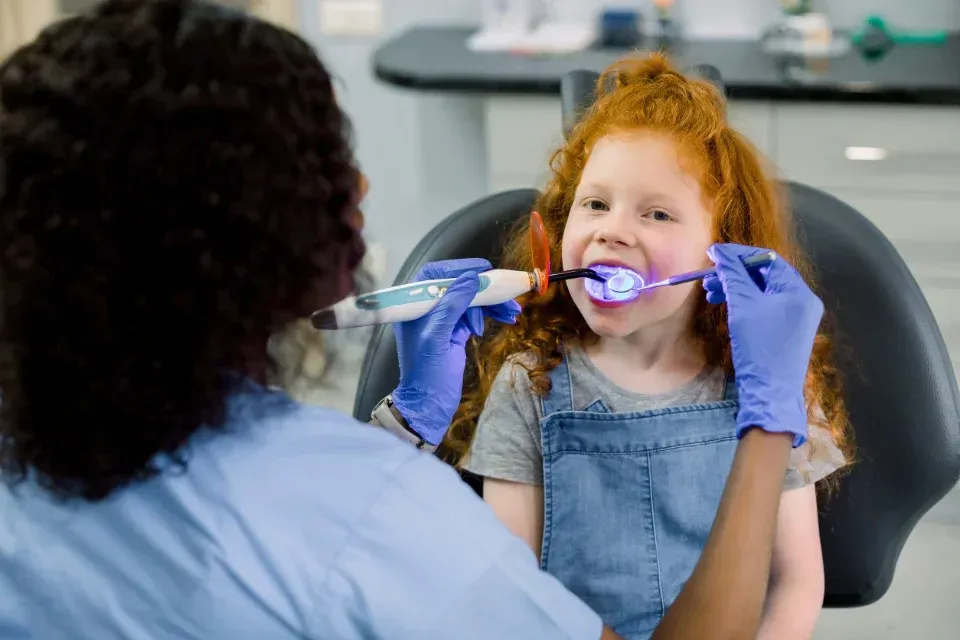 Un dentista le muestra a un niño cómo usar un cepillo de dientes azul-violeta en el sillón dental.