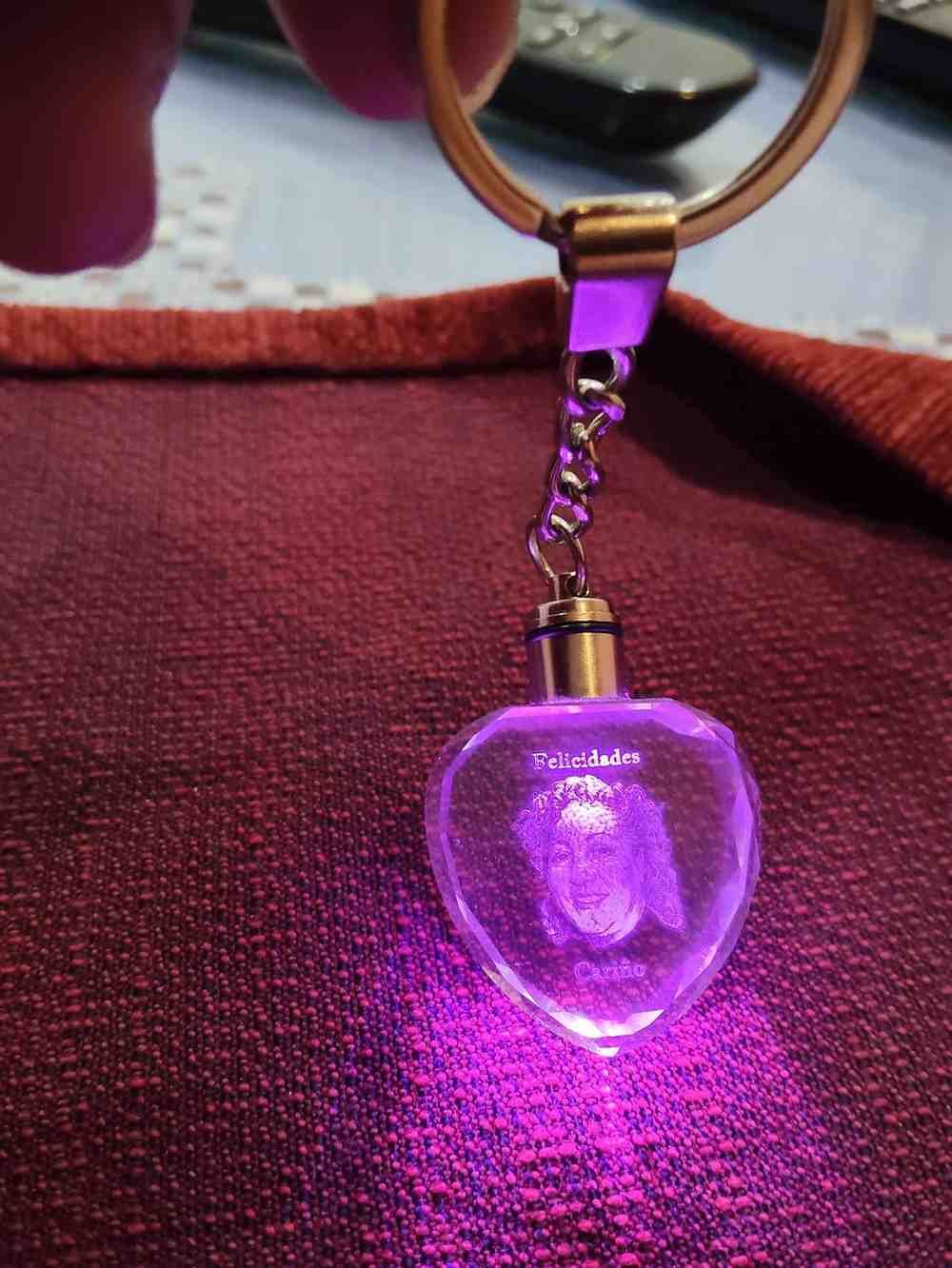 Llavero de cristal en forma de corazón iluminado con luz violeta; se ve un rostro dentro del cristal.