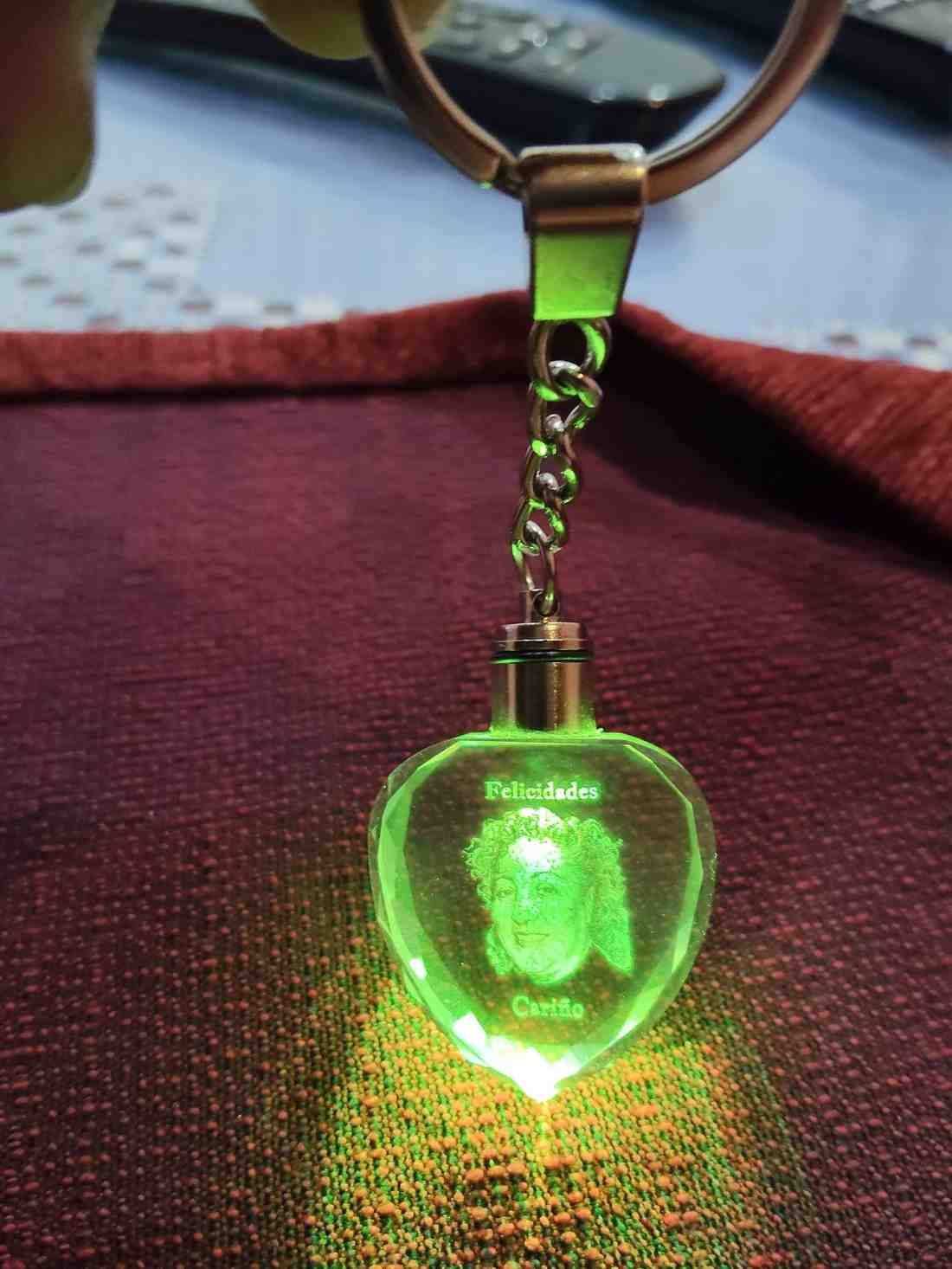 Llavero en forma de corazón verde brillante con retrato de perro, sobre una superficie roja.