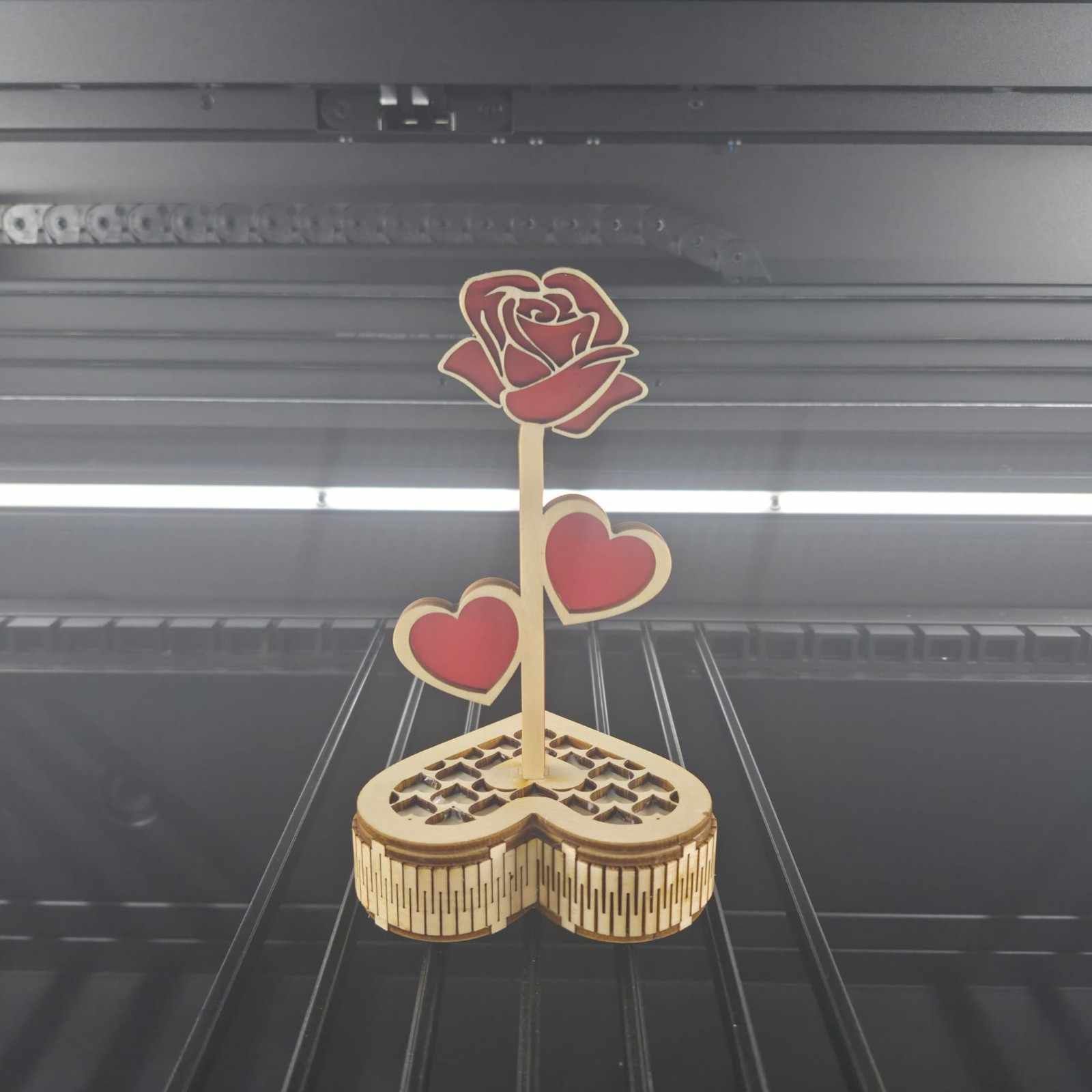 Decoración de rosa y corazón de madera cortados con láser con detalles rojos, sobre un fondo oscuro.