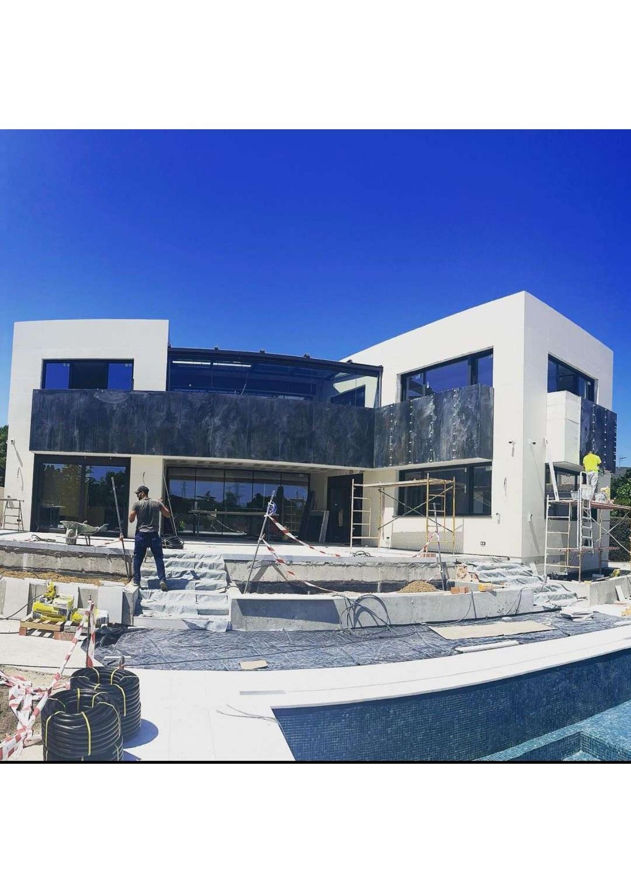 Se está construyendo una gran casa blanca al lado de una piscina.