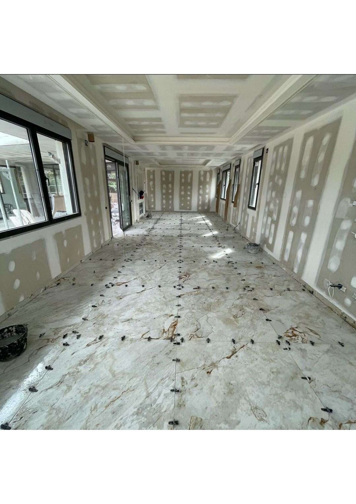 Una habitación grande con muchas ventanas y paneles de yeso en el piso.
