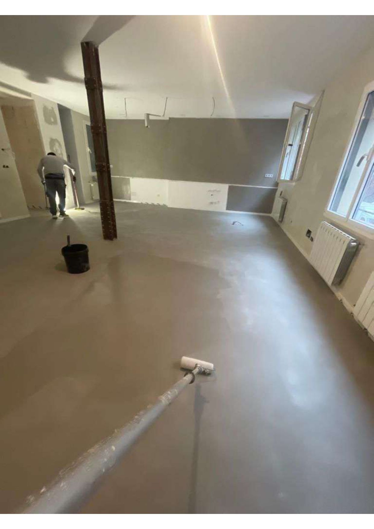 Un hombre está pintando el suelo de una habitación con un rodillo.