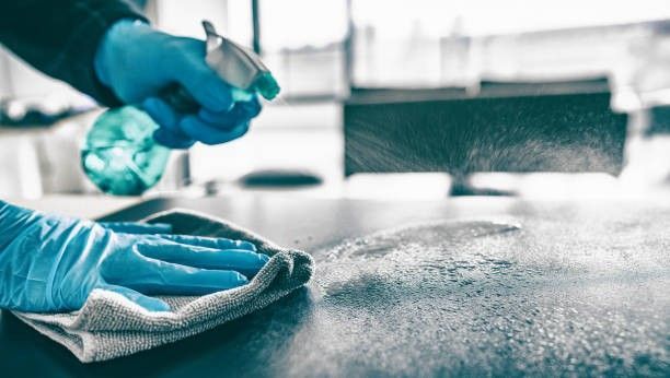 Mit behandschuhten Händen eine nasse Küchenarbeitsplatte mit Desinfektionsmittel besprühen und abwischen