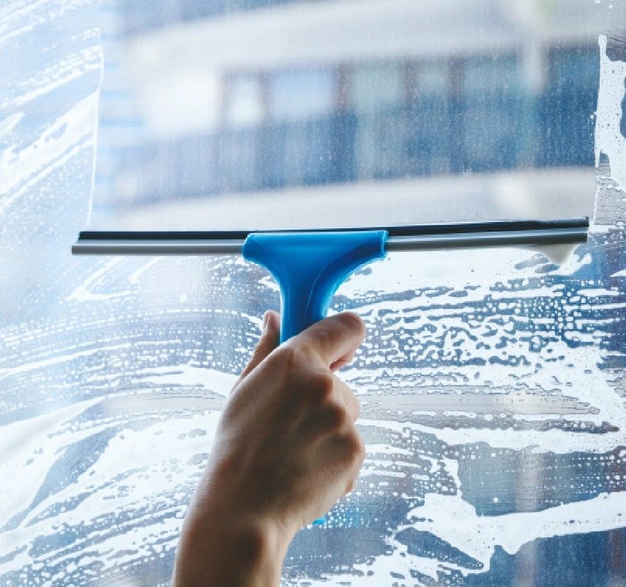 Eine Hand benutzt einen blauen Abzieher, um ein nasses Fenster zu reinigen.