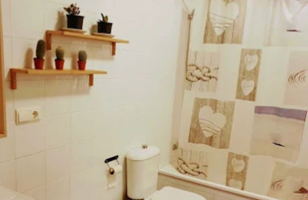 Un baño con inodoro, cortina de ducha y estantes.