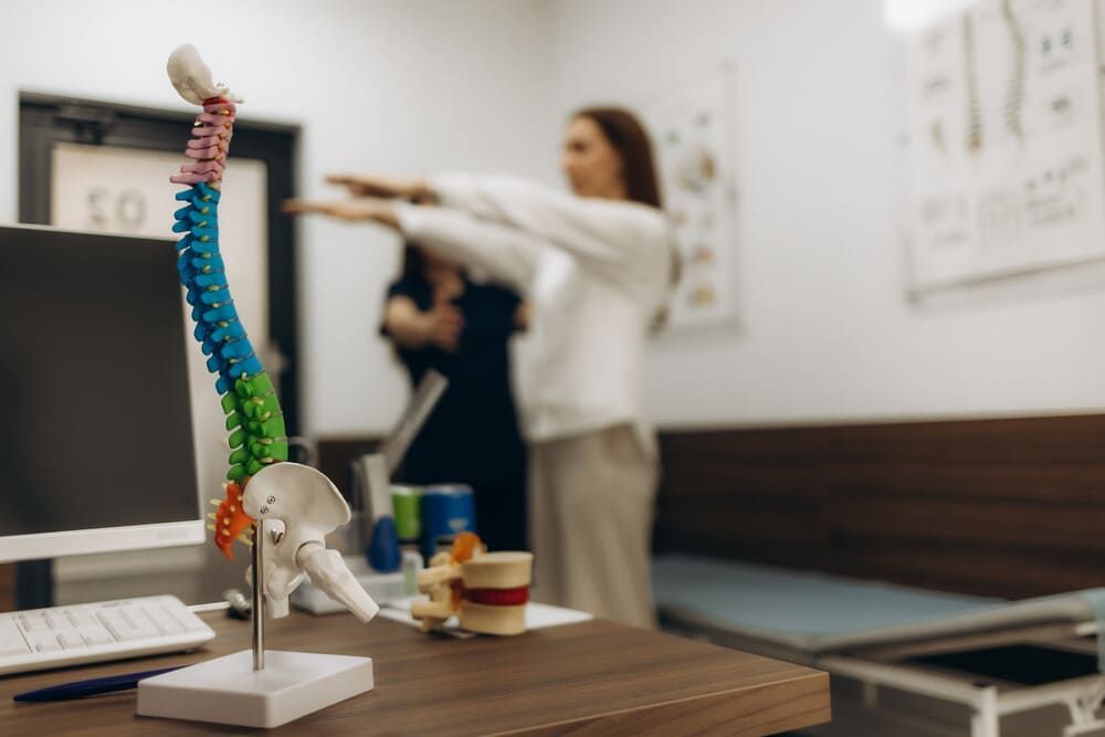 Una mujer estira los brazos delante de un modelo de columna vertebral.