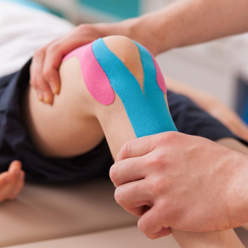 Una persona está colocando cinta kinesiológica en la rodilla de un niño.