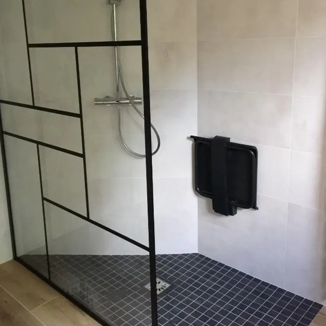 Douche moderne avec paroi à grille noire, carrelage blanc et tapis de sol en mosaïque foncée