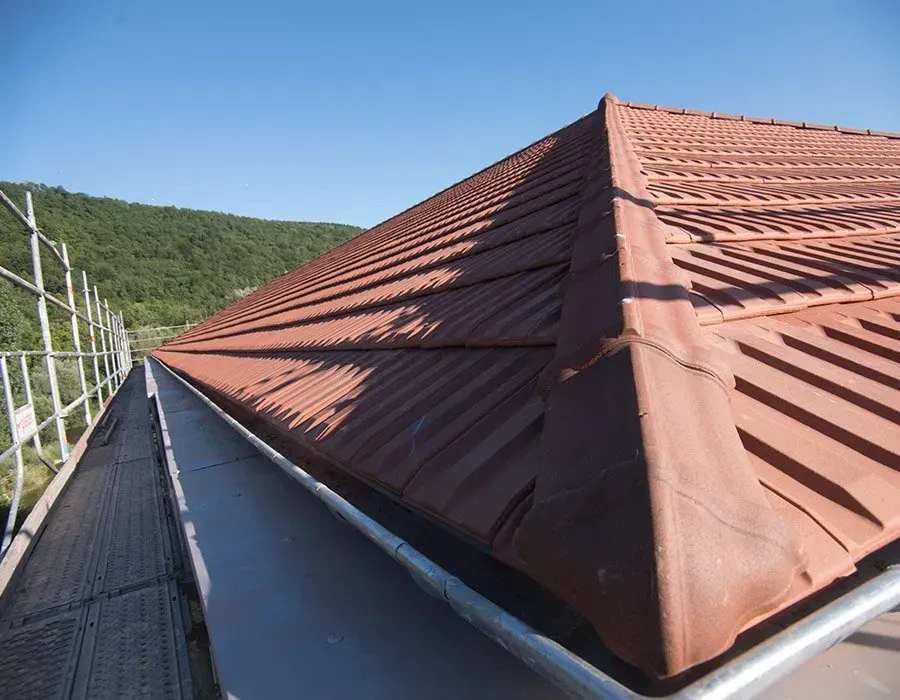 Faîtage d’un toit en métal rouge vu depuis une passerelle d’échafaudage, à flanc de colline sous un ciel bleu