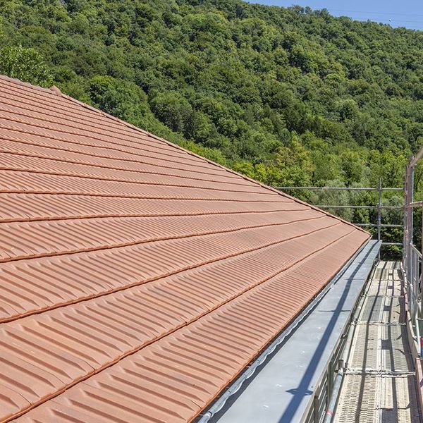 Toit métallique couleur cuivre, près d’un versant boisé, avec une passerelle d’échafaudage