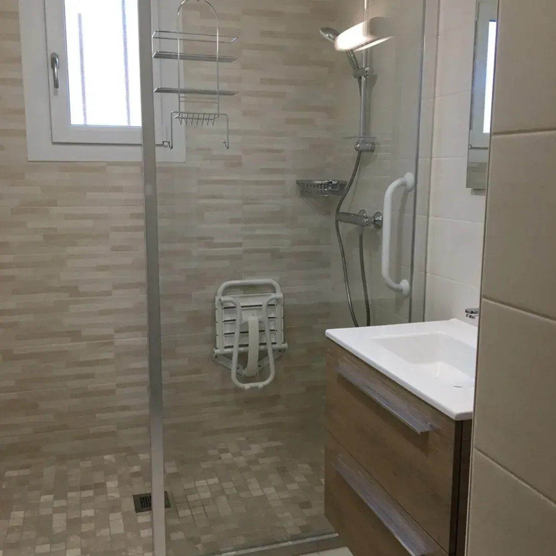 Salle de bains accessible avec douche à l’italienne, barres d’appui, siège de douche et lavabo mural