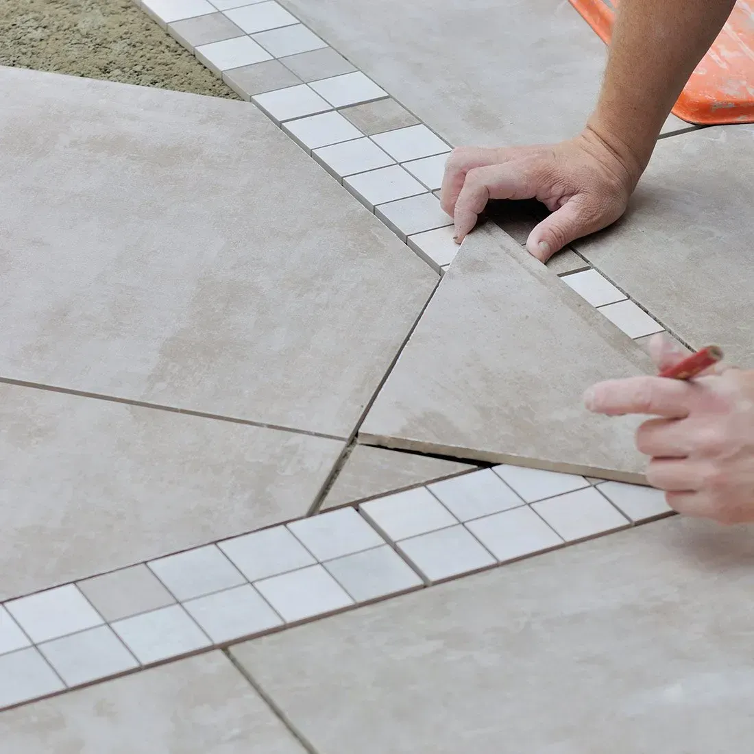 Des mains ajustant une pièce de carrelage triangulaire dans un motif de sol carrelé