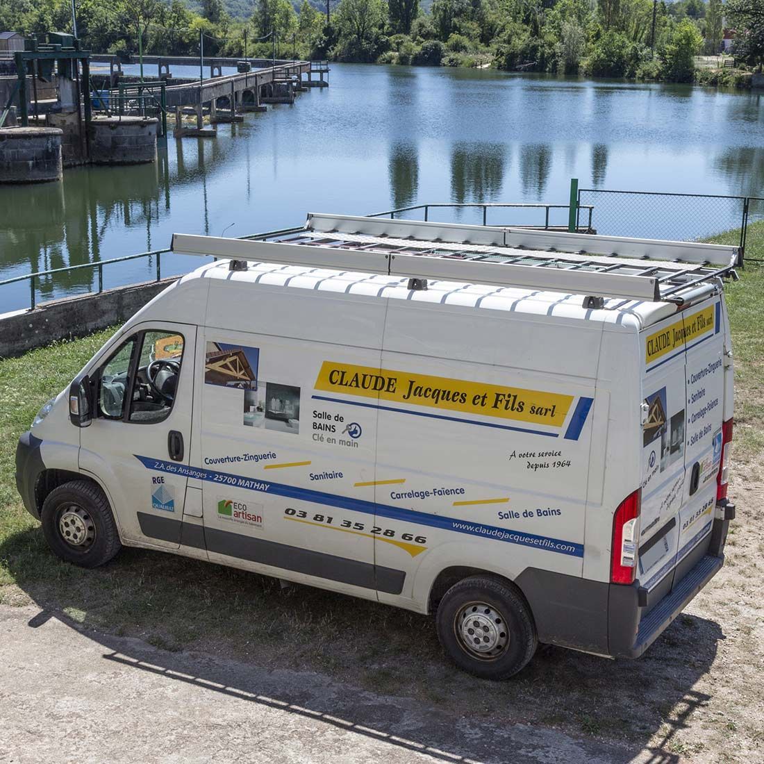 Fourgon de service blanc garé au bord de l’eau, près des quais et des arbres