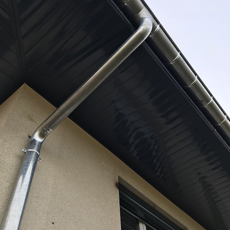 Une descente pluviale et une gouttière en métal sur la façade d’une maison, sous le bord sombre du toit