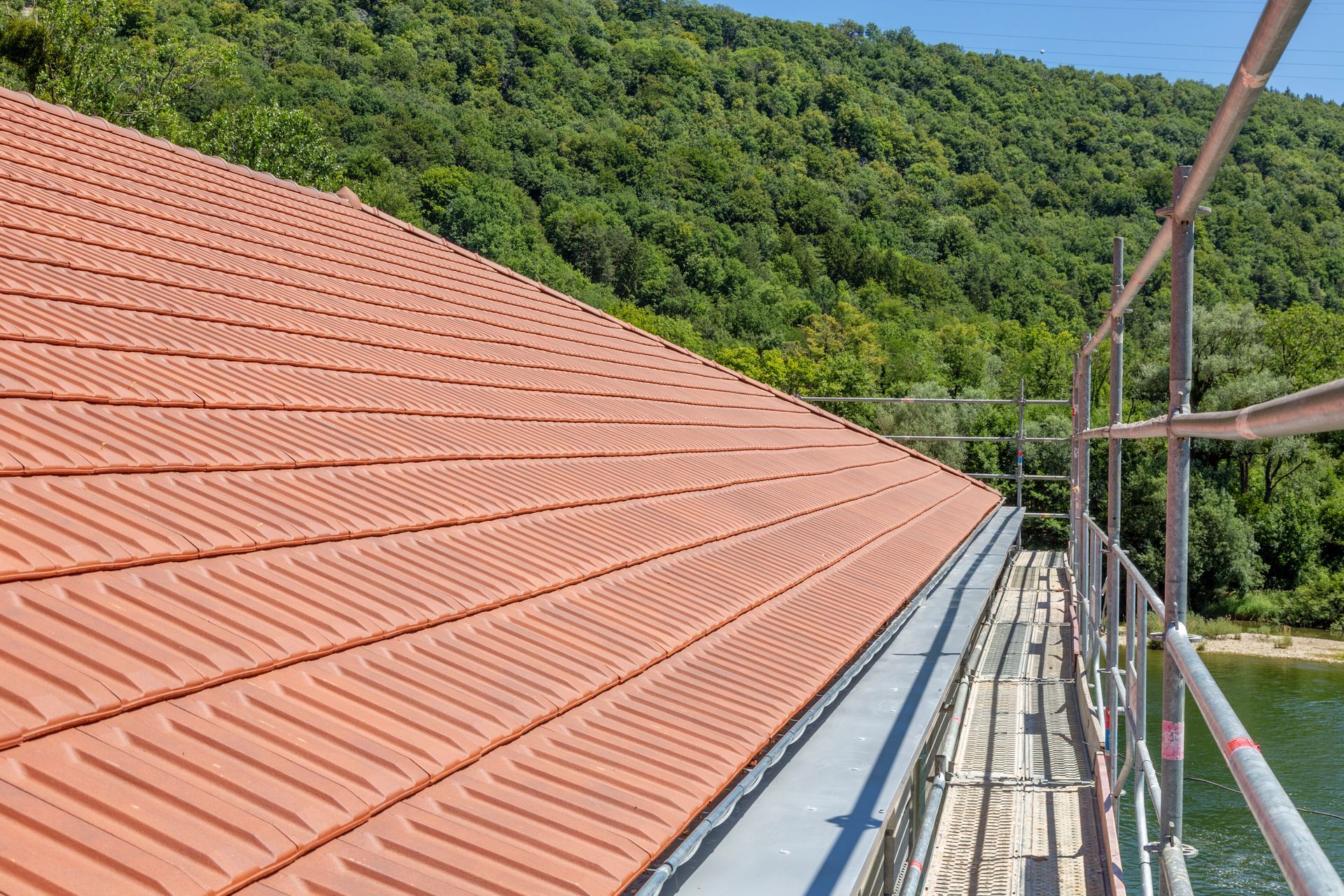 Toit en tuiles rouges en construction, avec un échafaudage près d’une colline verdoyante et boisée