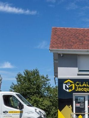 Camionnette blanche à côté d’un magasin au toit de tuiles rouges, sous un ciel bleu dégagé