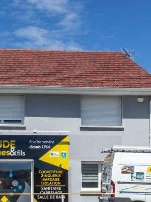 Façade de maison grise avec un toit en tuiles rouges et une camionnette blanche garée devant