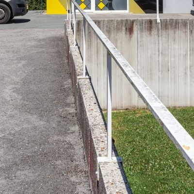 Borne de stationnement en béton à côté d’un revêtement asphalté, avec une rambarde métallique et une bande de pelouse