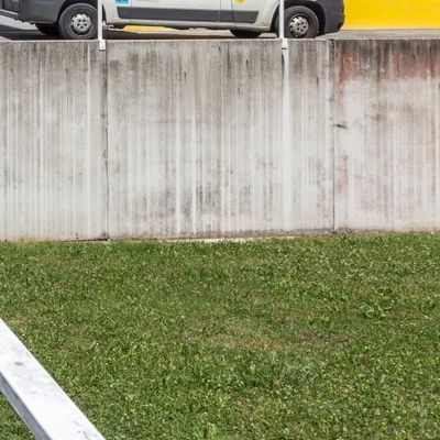 Mur de soutènement en béton blanc au-dessus d’un talus verdoyant, avec le côté d’un véhicule garé visible en haut