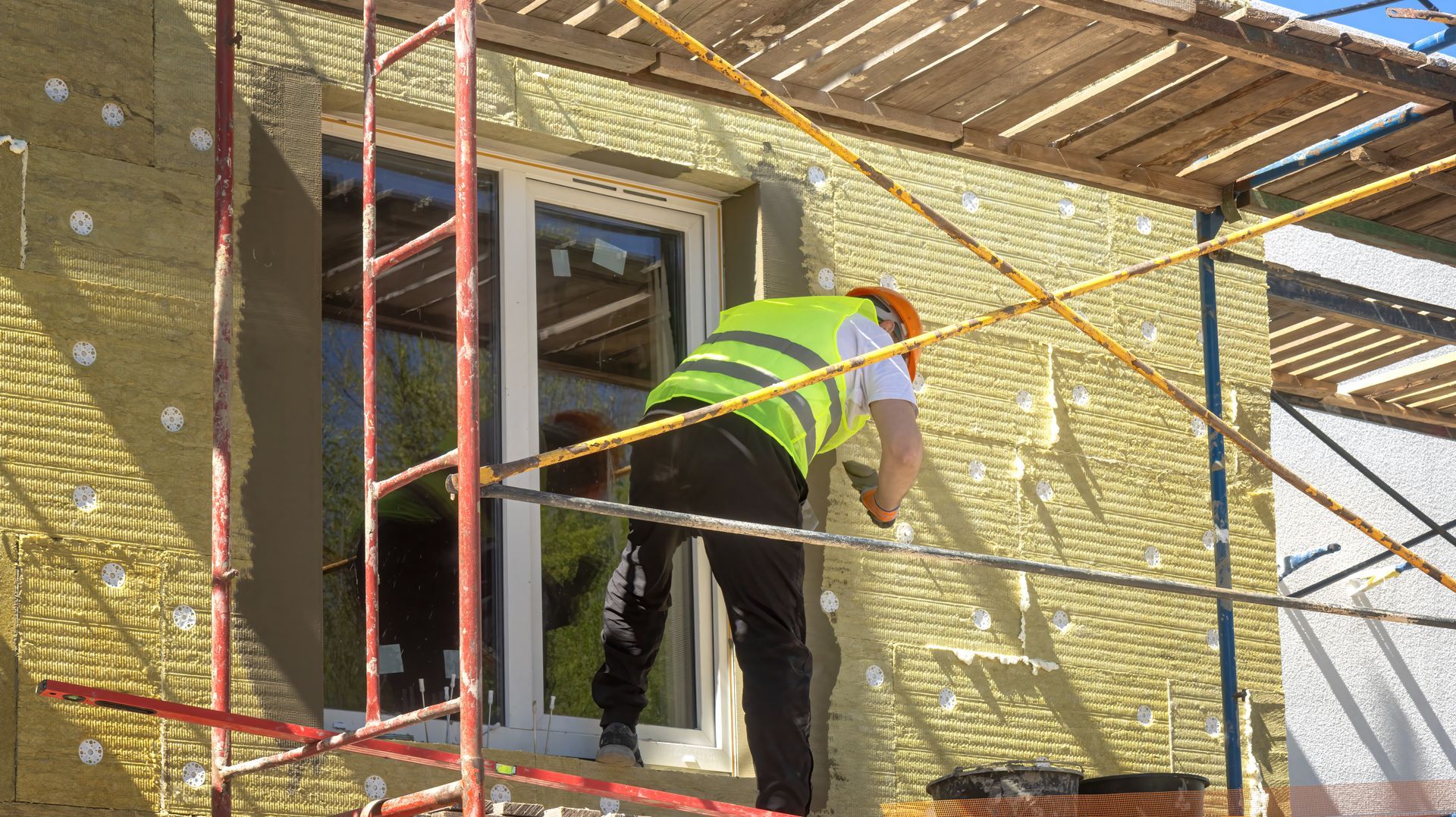 Un ouvrier portant un gilet de sécurité fluorescent travaille sur un échafaudage, le long de la façade d’un bâtiment