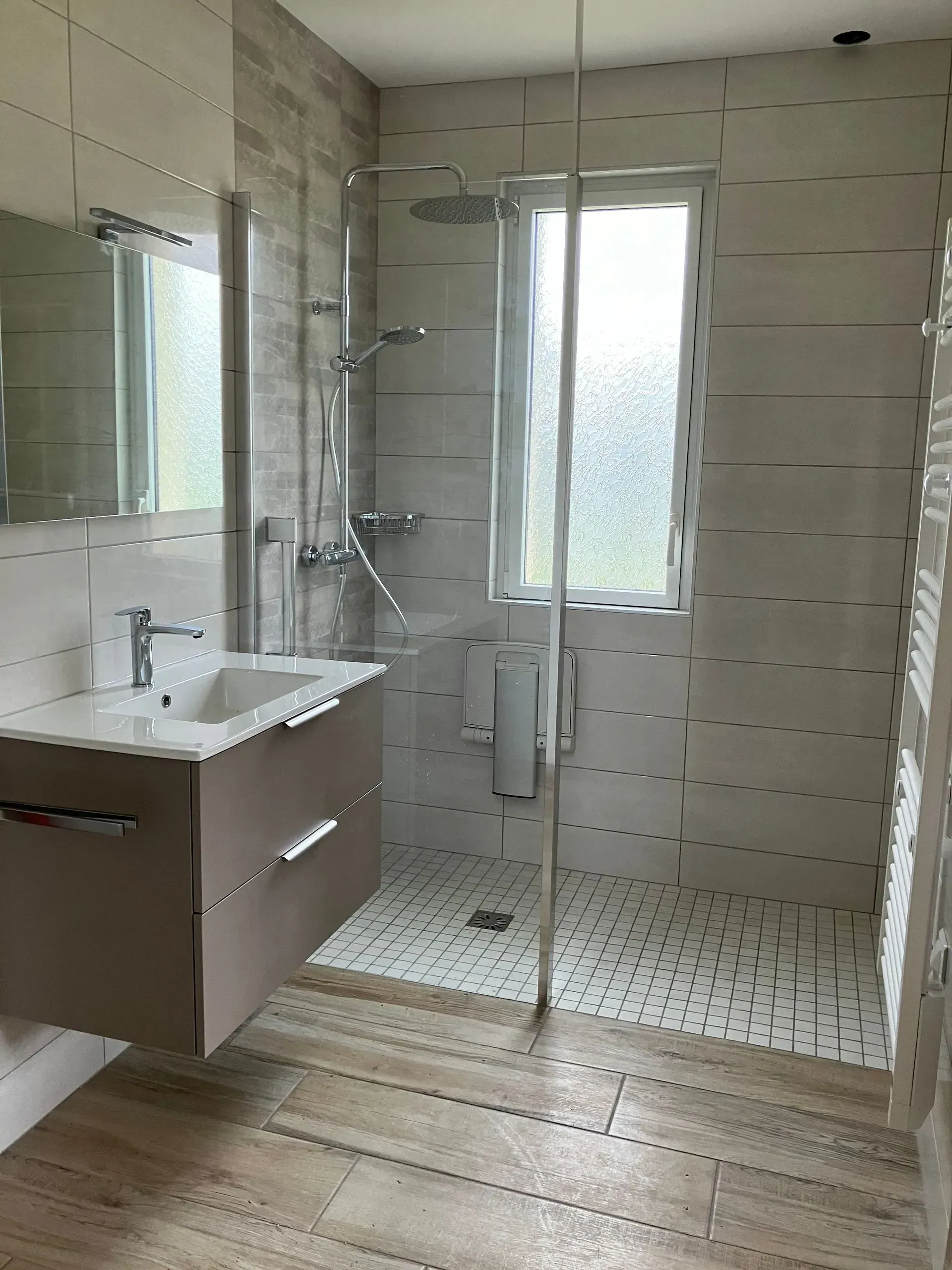 Salle de bains moderne avec douche vitrée, lavabo mural et sol en carrelage imitation bois