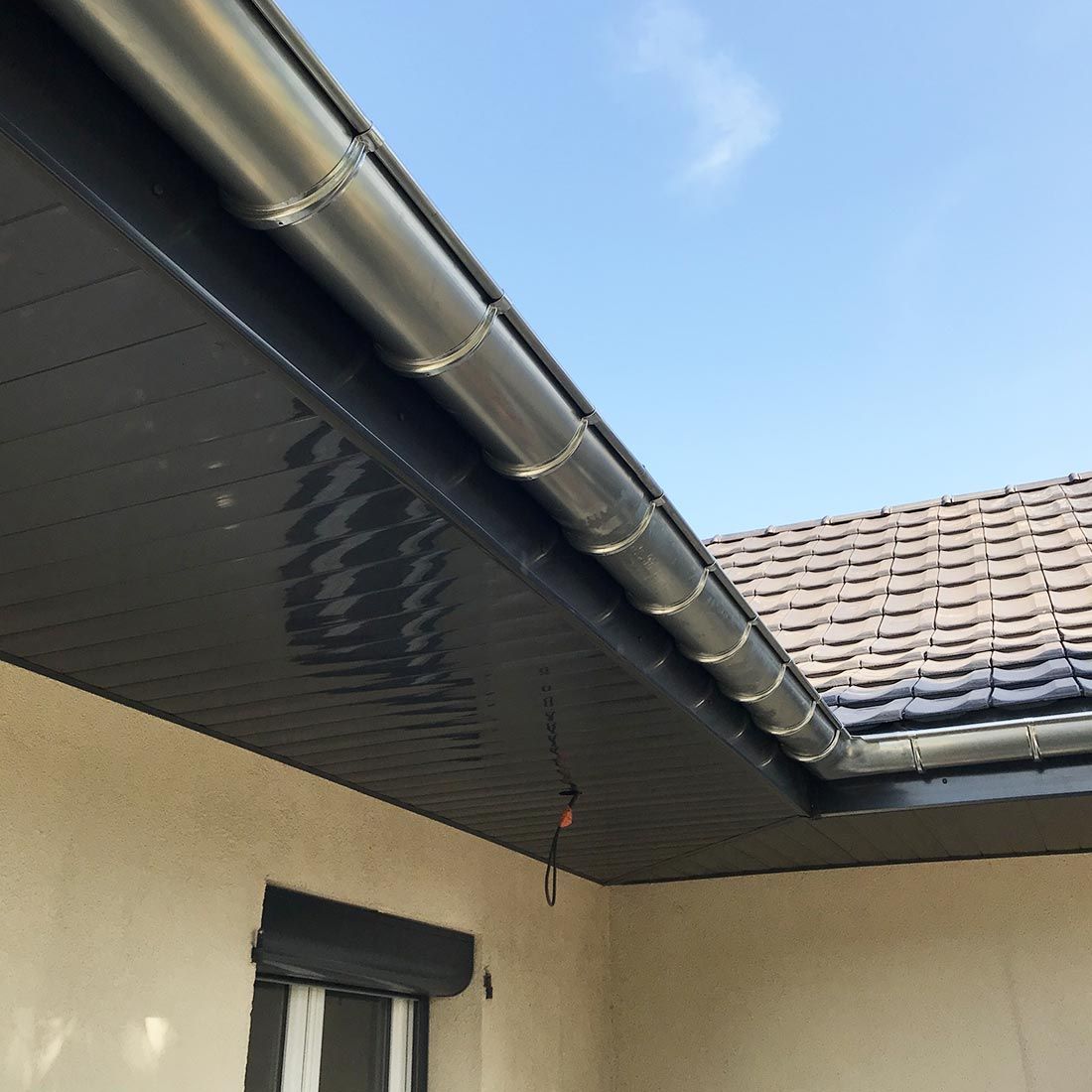 Angle du toit d’une maison avec des gouttières foncées, des murs beiges et un ciel bleu en arrière-plan