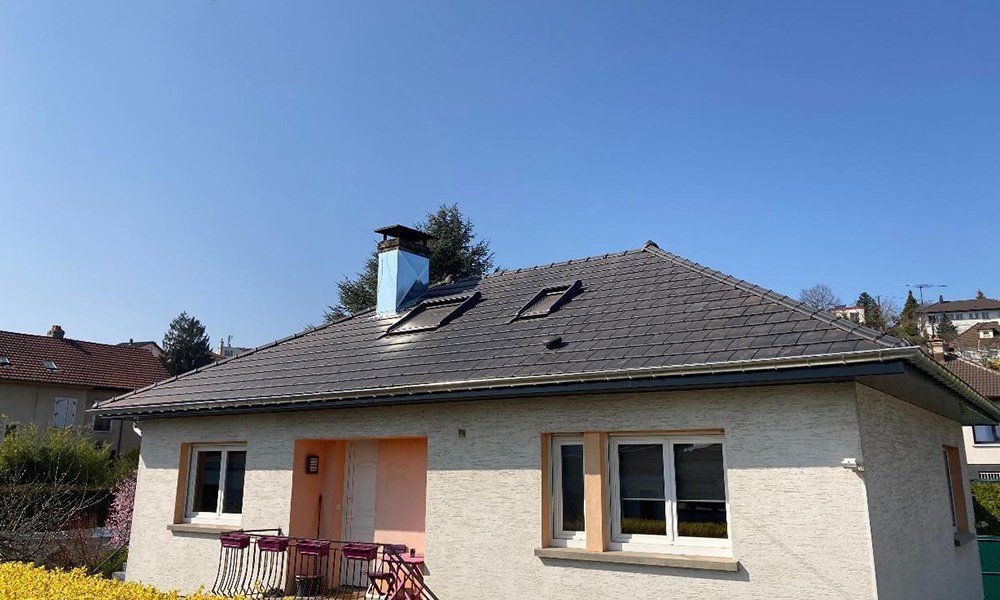 Maison de plain-pied avec un toit sombre, une cheminée et une rambarde rouge sous un ciel bleu dégagé