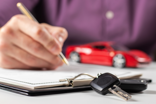 Una persona sta scrivendo su un blocco per appunti con una penna davanti a un'auto rossa.