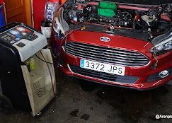 Automóvil Ford rojo con el capó abierto, recibiendo mantenimiento de un aparato de aire acondicionado en un taller de reparación.