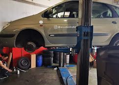 Un coche subido a un elevador en un garaje; un mecánico trabaja en él.