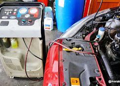 El compartimiento del motor de un automóvil rojo recibe mantenimiento mediante una máquina de recarga de CA en un taller.