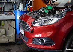 Coche rojo con el capó abierto en un taller mecánico; motor visible.