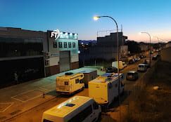 Escena callejera al anochecer con furgonetas estacionadas, edificios y farolas. Logotipo de FT en un edificio.