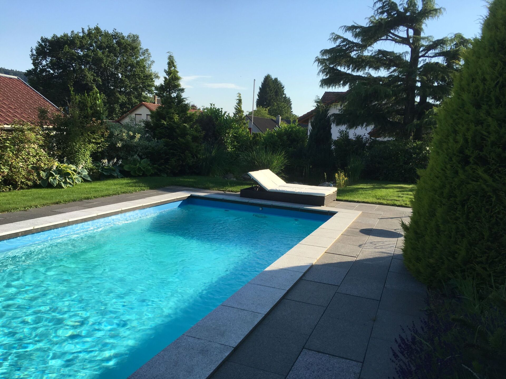 Blauer, gefliester Pool mit Fliesenarbeit vor einem gepflegten Garten