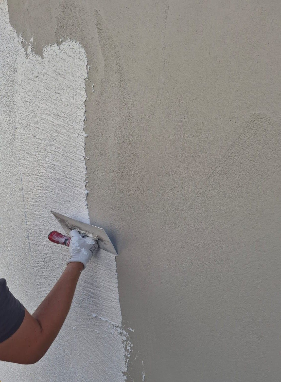 Ein Arbeiter trägt in Handschuhen und Overall mit einer Kelle weißen Putz an eine Wand auf.