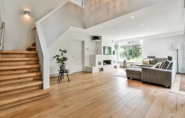 Helles, modernes Wohnzimmer mit Holzboden, grauem Sofa, Treppe und großem Fenster mit Blick ins Grüne