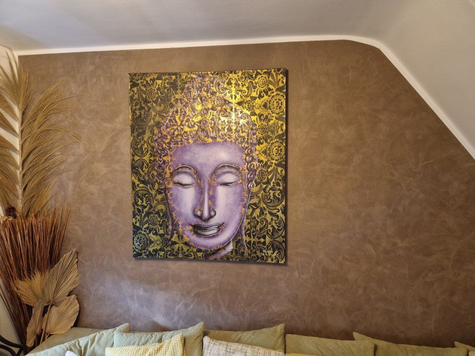 Abstraktes Buddha-Gesichtsgemälde an einer hellbraunen Wand über dekorativen Trockenpflanzen in einem gemütlichen Zimmer