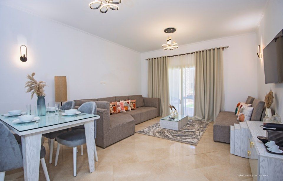Helles, modernes Wohn-Esszimmer mit grauen Sofas, Glasesstisch und Schiebetüren zu einem Balkon.