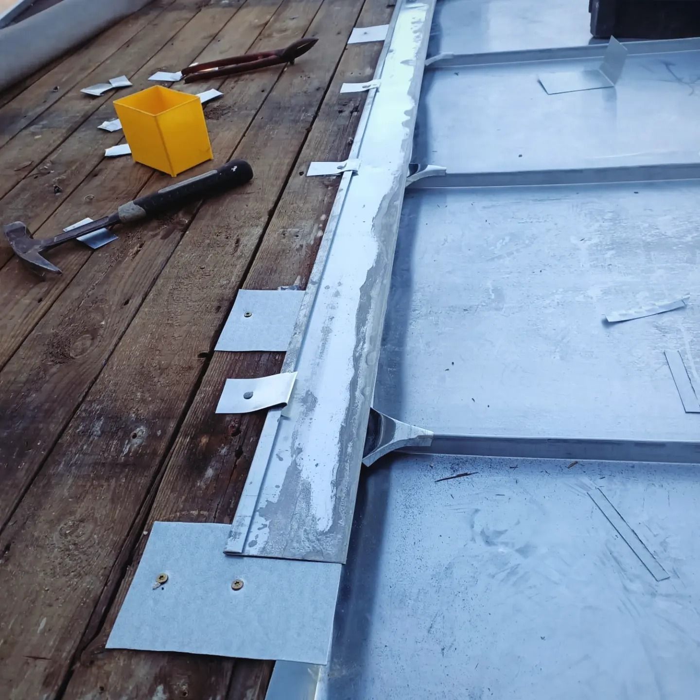 Gros plan sur un toit avec une partie en bois et une partie en zinc avec des outils