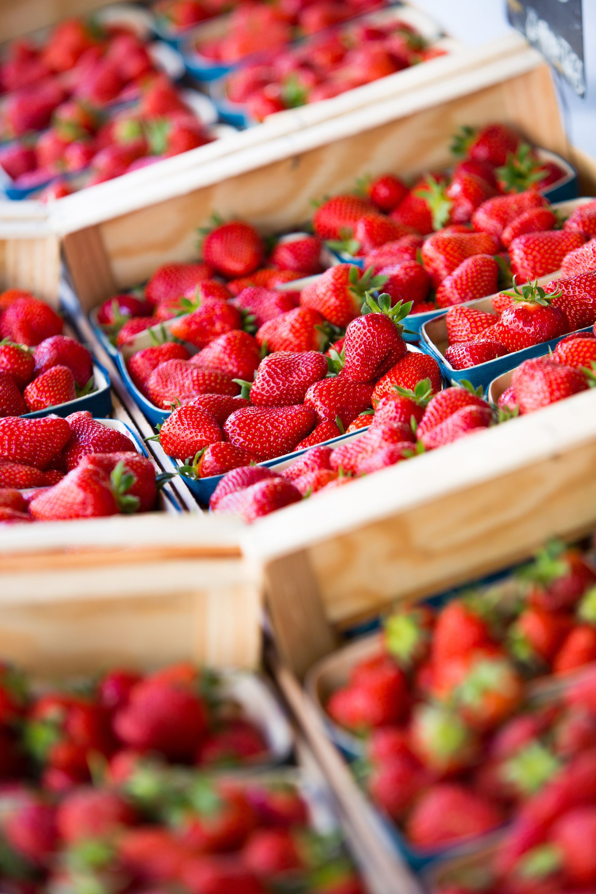 Des caisses en bois débordant de fraises rouges mûres sur un marché.