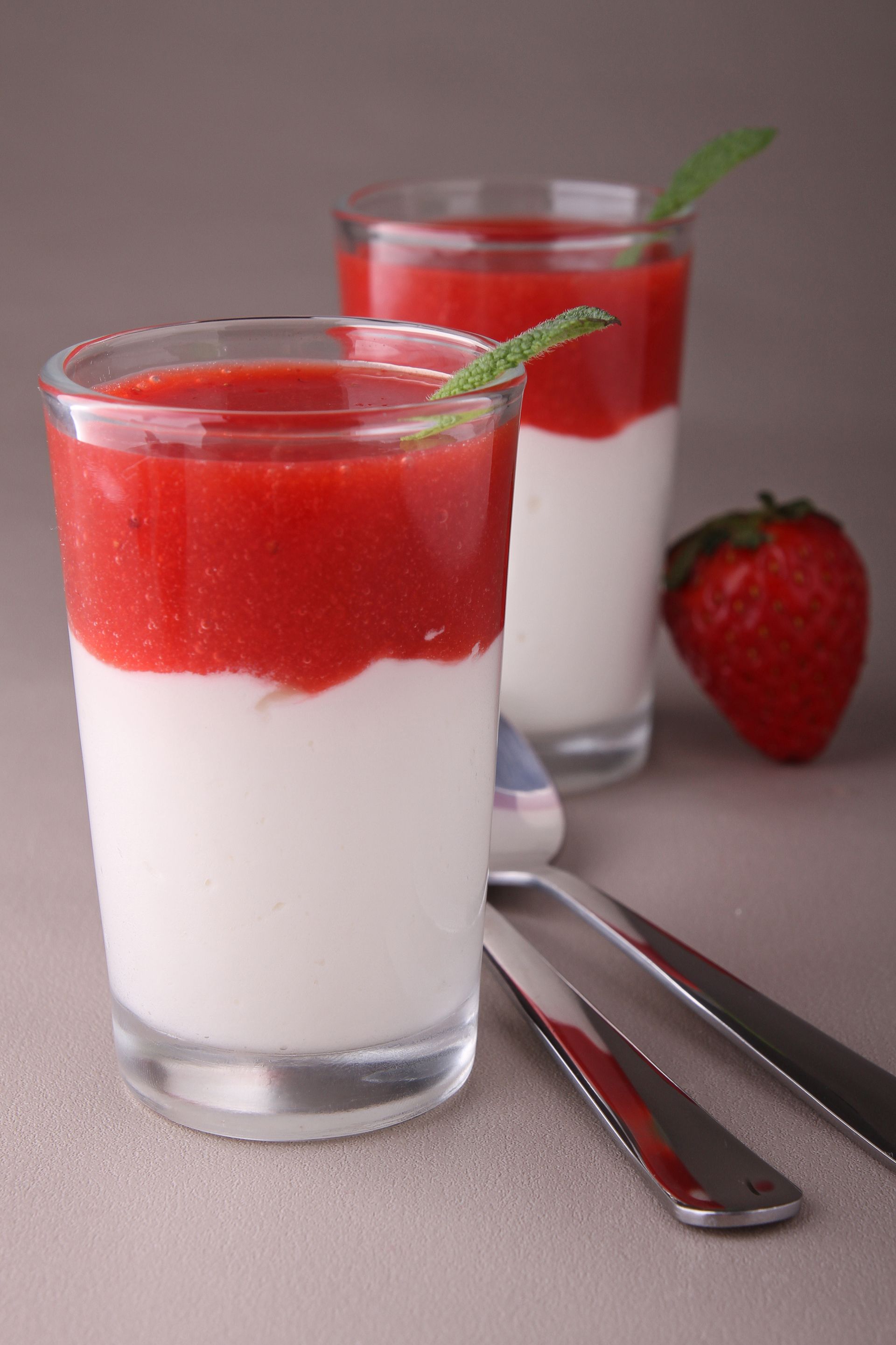 Deux desserts aux fraises présentés dans des verrines et garnis de menthe. Une couche de purée de fraises rouges sur une couche de crème blanche.