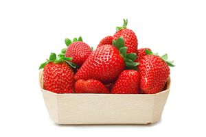 Fraises dans un petit panier en bois clair. Baies rouges et feuilles vertes sur fond blanc.
