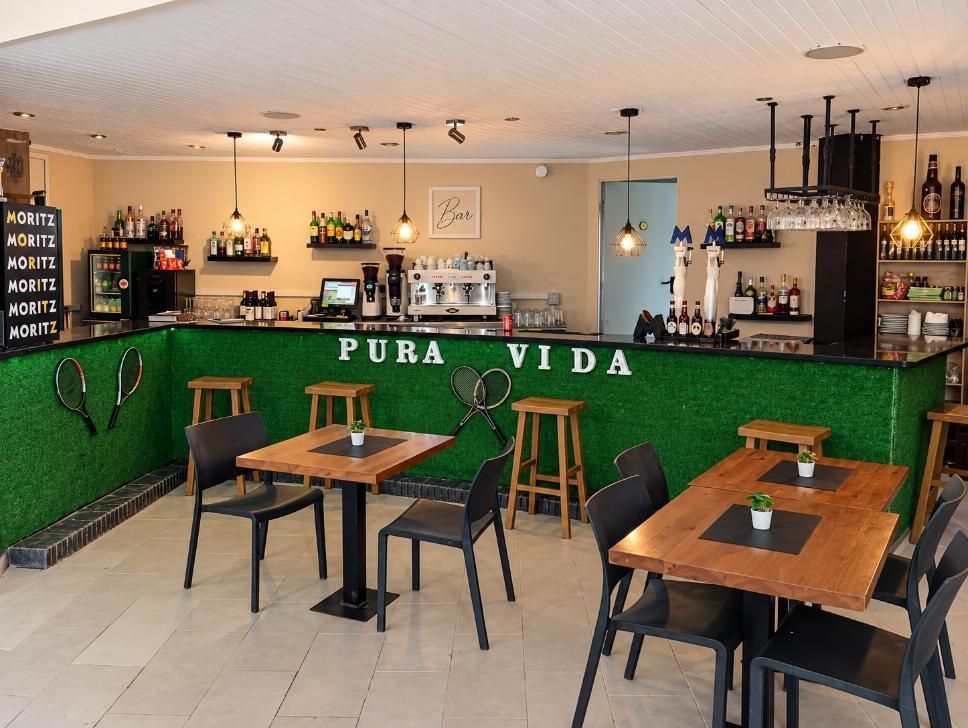 Interior acogedor de un bar con barra verde, mesas de madera, taburetes y botellas en las estanterías