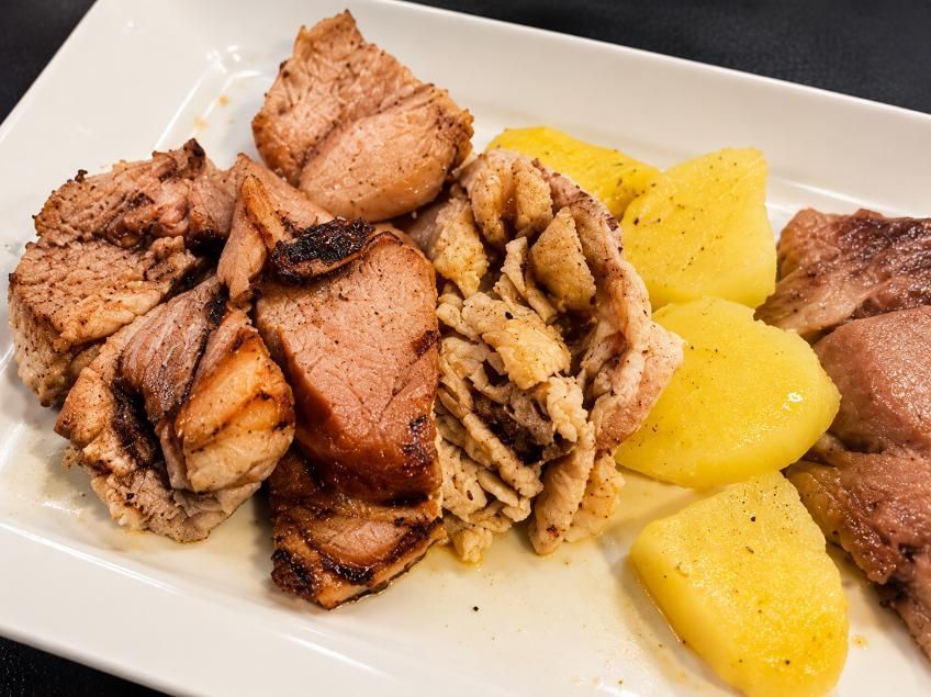 Plato de trozos de carne a la parrilla con pedazos de papa amarilla en un plato blanco